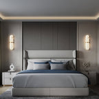 Clérachic pill sconce mounted on a panelled charcoal wall beside a low bed in a calm grey bedroom.
