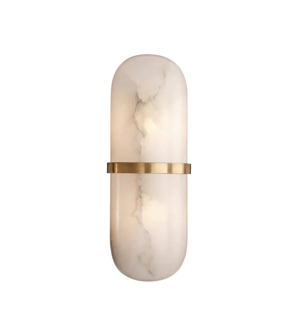 The Clérachic wall lamp switched on, brass band catching the light while the alabaster body glows softly.