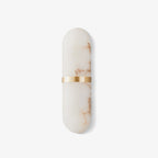 Clérachic alabaster wall lamp on a pale grey ground, rust-toned veining threading through the stone.