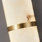 Macro of the Clérachic sconce's brushed brass band crossing the lit alabaster body, grain visible in the metal.