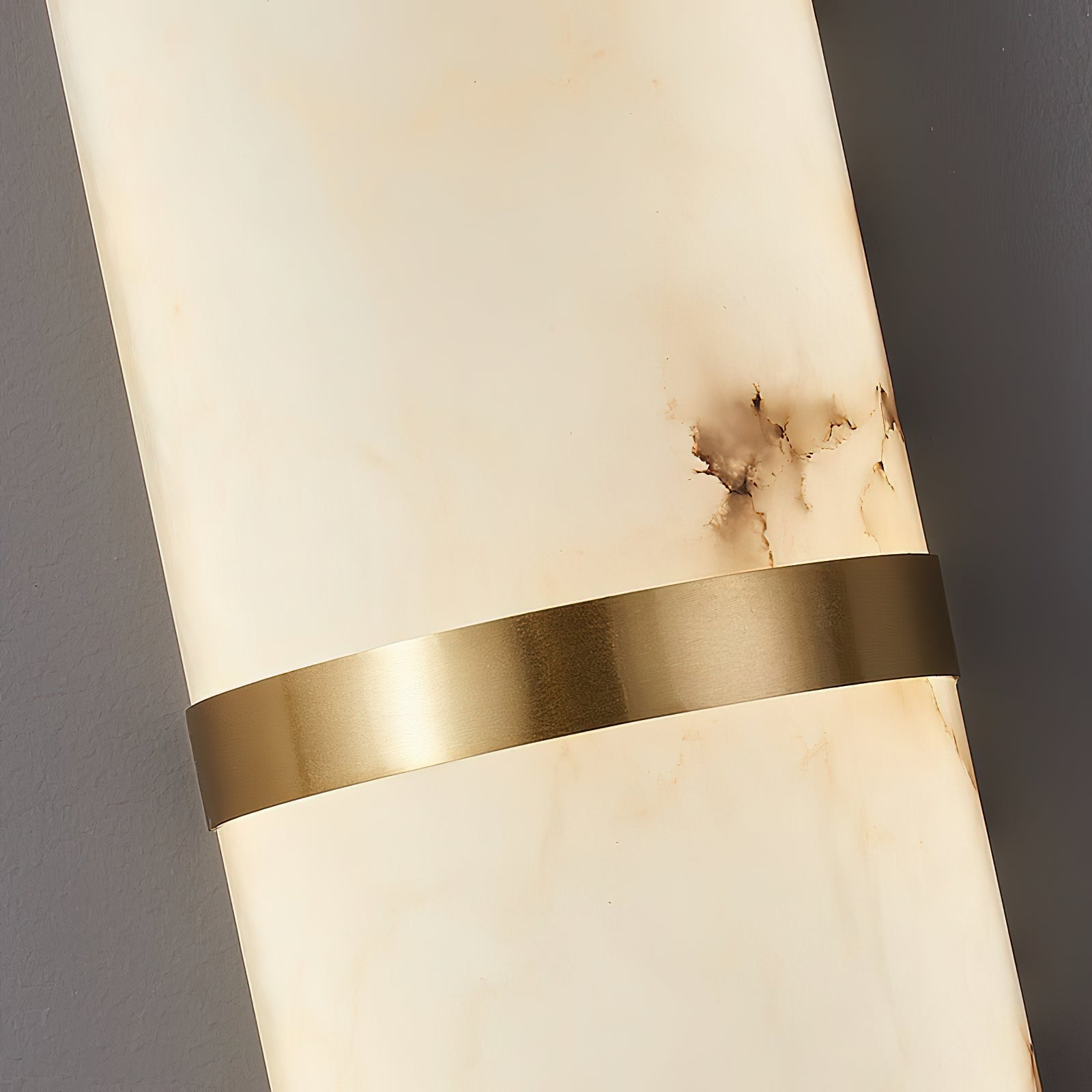 Macro of the Clérachic sconce's brushed brass band crossing the lit alabaster body, grain visible in the metal.