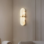 The Clérachic sconce lit on a pale wall above the curved rim of a freestanding bath in a calm bathroom.