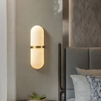 Clérachic pill lamp casting warm light down a taupe bedroom wall next to an upholstered headboard.