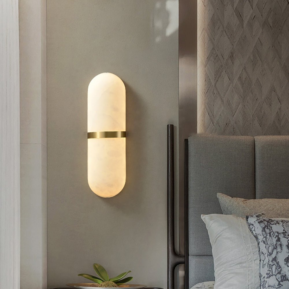 Clérachic pill lamp casting warm light down a taupe bedroom wall next to an upholstered headboard.