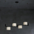The Clérachic Ostruvye in its four-light bar, alabaster cubes stepped along a slim arm against a grey concrete wall.