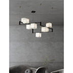 Clérachic chandelier suspended over a curved grey sofa, its alabaster boxes glowing against a concrete wall.