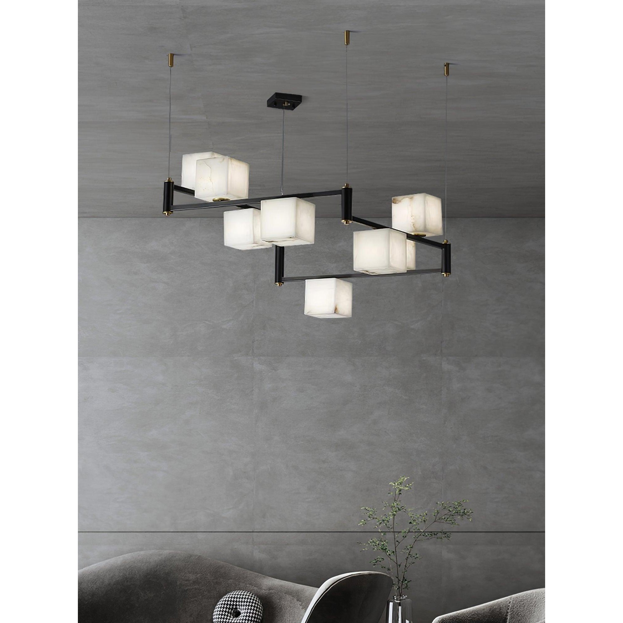 Clérachic chandelier suspended over a curved grey sofa, its alabaster boxes glowing against a concrete wall.