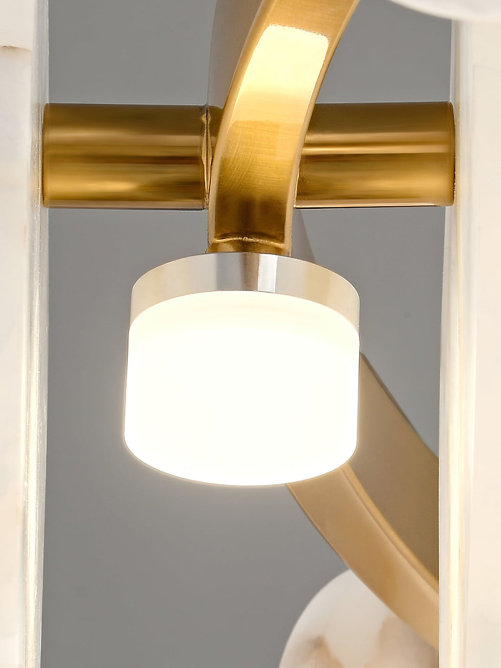 Clérachic detail of a brass arm joint, the cylindrical opal glass shade lit warm beneath a polished brass collar.