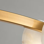 The Clérachic chandelier's brushed brass band close up, its satin grain curving past a translucent alabaster disc.