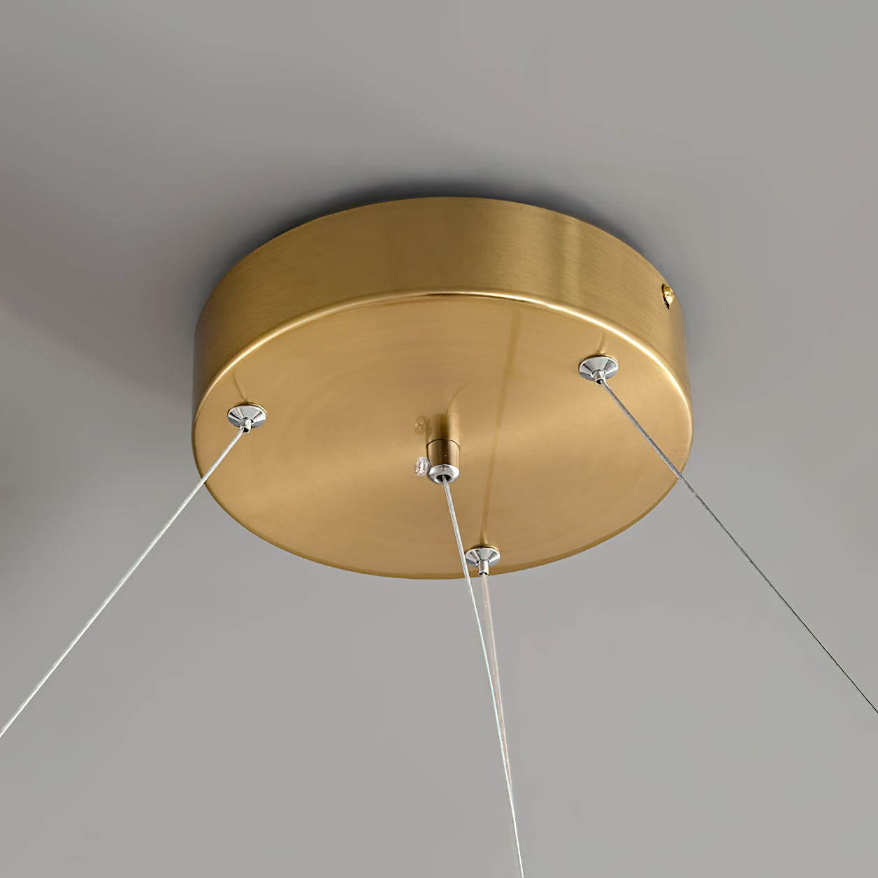 Clérachic round brass ceiling canopy seen from below, with three fine suspension cables anchored at its rim.