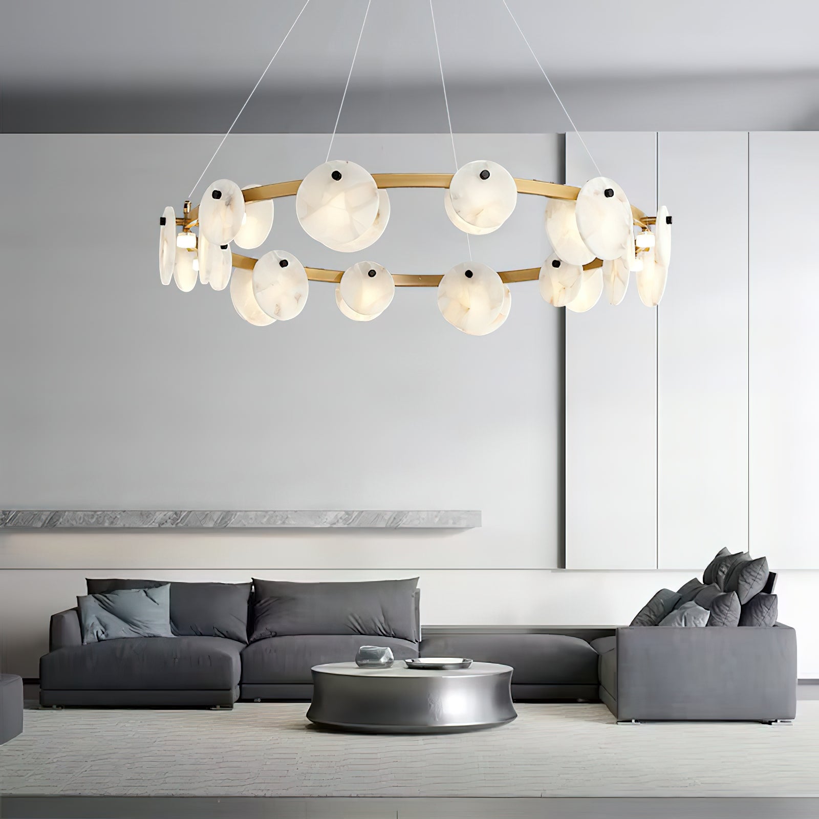 The Clérachic chandelier hung over a grey sectional sofa, its brass ring floating in a pale open living room.