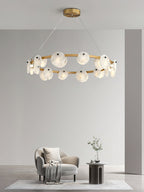 The Clérachic chandelier lighting a spare room with a cream armchair and a slim side table below its brass ring.