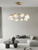 Clérachic chandelier centred over a grey sofa and a dark round stone table, its alabaster discs warm-lit.