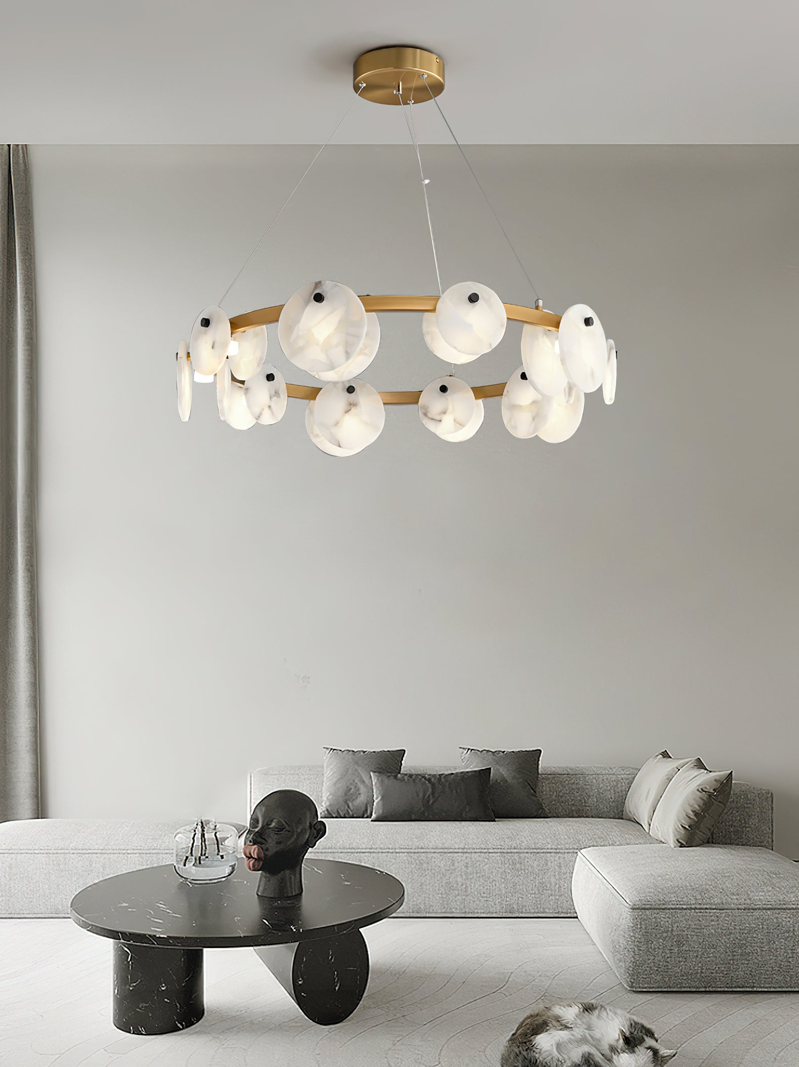 Clérachic chandelier centred over a grey sofa and a dark round stone table, its alabaster discs warm-lit.