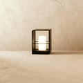 Clérachic small black lantern with a glowing white candle-style cylinder, standing on a pale stone floor against a limewash wall.