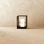 Clérachic small black lantern with a glowing white candle-style cylinder, standing on a pale stone floor against a limewash wall.