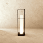 Clérachic tall black lantern with a long glowing white cylinder inside a slim open frame, shown against a textured wall.