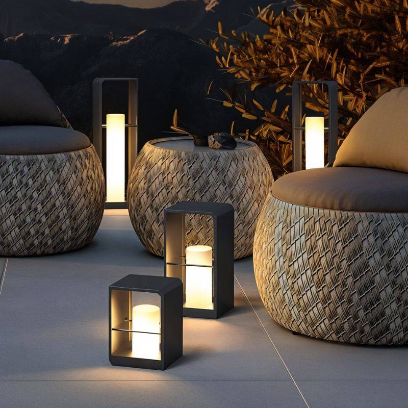 Clérachic black lanterns in three heights glowing warm on a patio among woven lounge chairs, with hills at dusk behind.