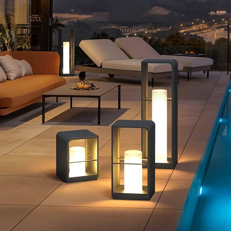 Clérachic dark lanterns in three heights glowing beside a terrace pool, with sun loungers and an orange sofa at dusk.