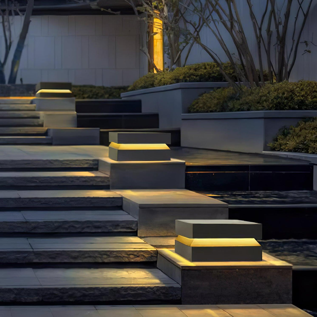 Along a stone stairway at dusk, Clérachic square post lights sit on the steps and glow warm.