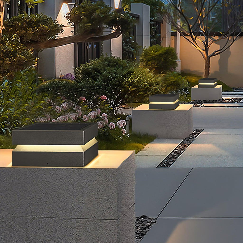 In a planted courtyard at dusk, a Clérachic post light sits on a pale block with more along the path.