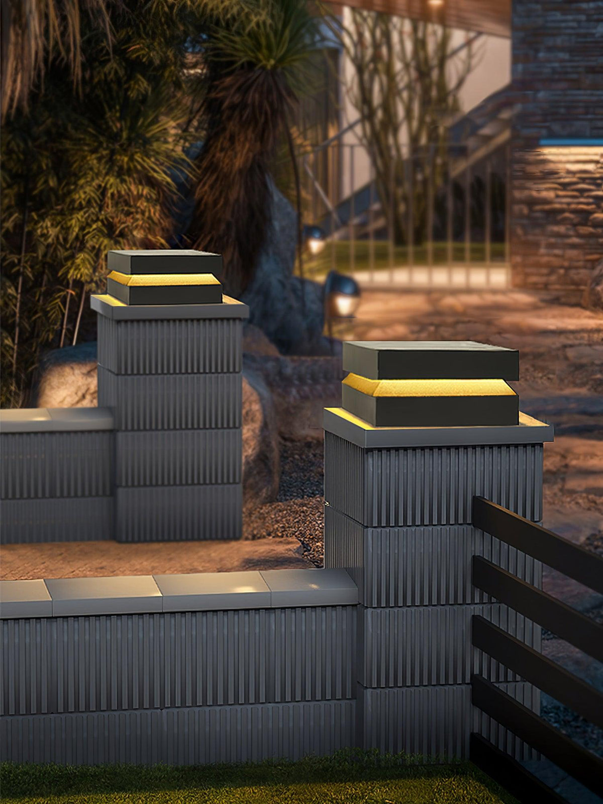 Clérachic post lights on two ribbed wall pillars beside a slatted fence, lit warm in the evening.