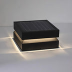 Clérachic square post light with its warm light cast across a pale surface and a solar panel on top.