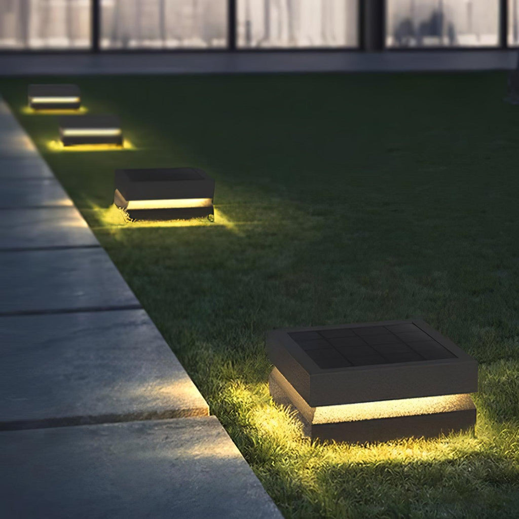 A line of Clérachic post lights marks a lawn edge beside a stone path, each glowing warm at night.