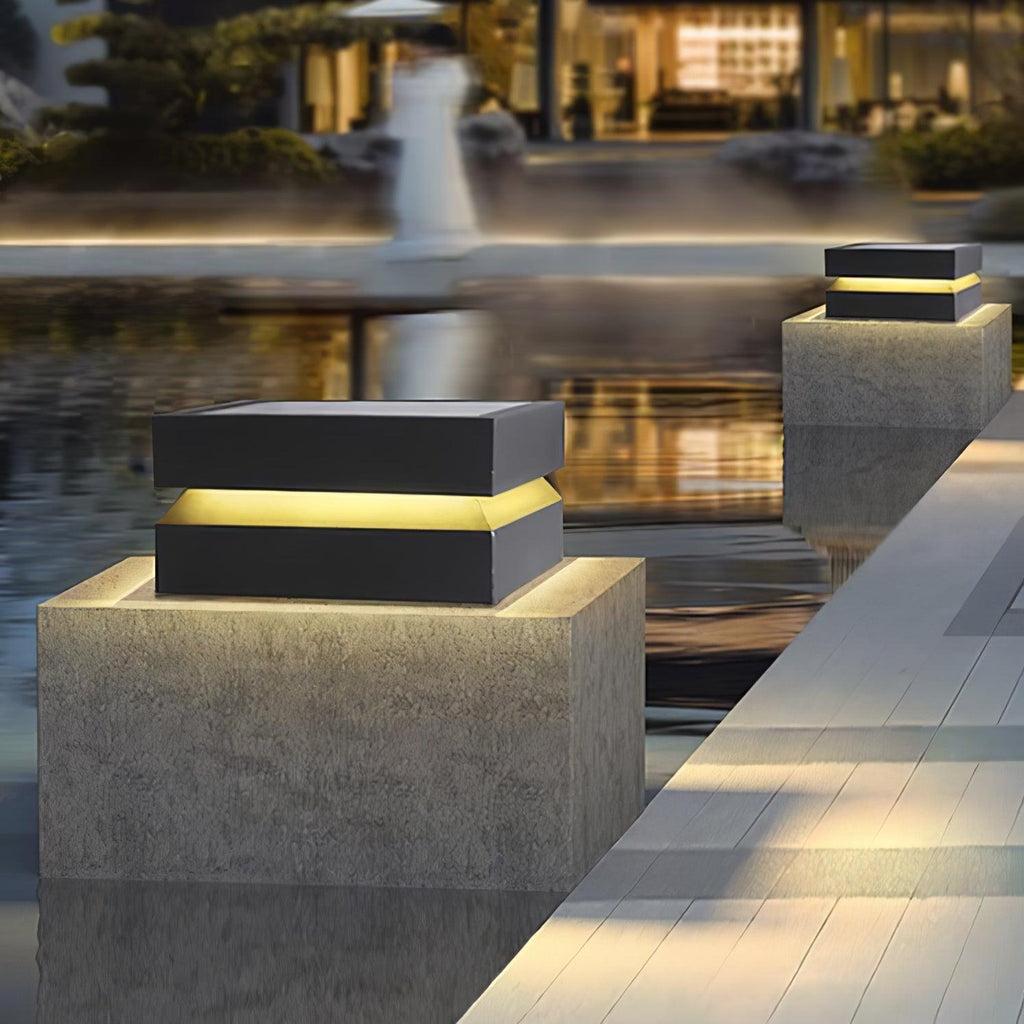 Lit Clérachic post light on a textured concrete pier at water level, with a glowing building beyond.