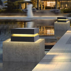 Lit Clérachic post light on a textured concrete pier at water level, with a glowing building beyond.