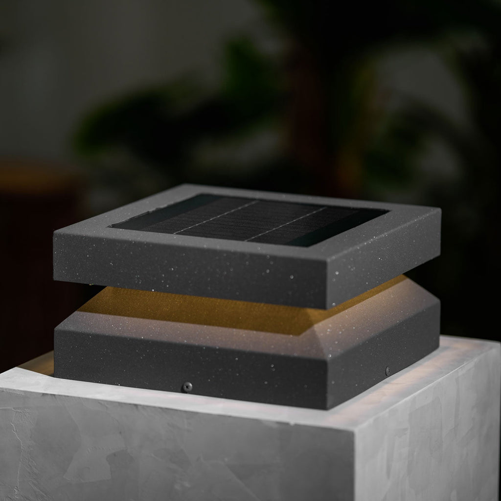 Close view of a Clérachic post light on a stone block, speckled dark grey metal and a faint warm glow.