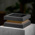 Close view of a Clérachic post light on a stone block, speckled dark grey metal and a faint warm glow.