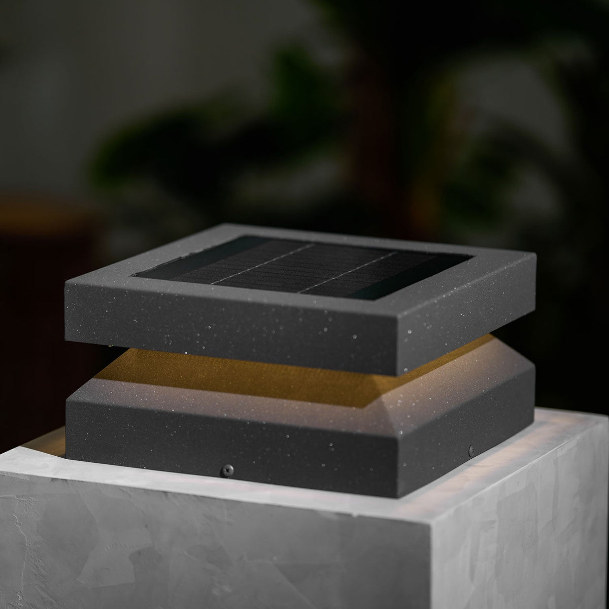 Close view of a Clérachic post light on a stone block, speckled dark grey metal and a faint warm glow.