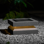 Clérachic post light resting on grey gravel at night, a warm amber glow between lid and base.