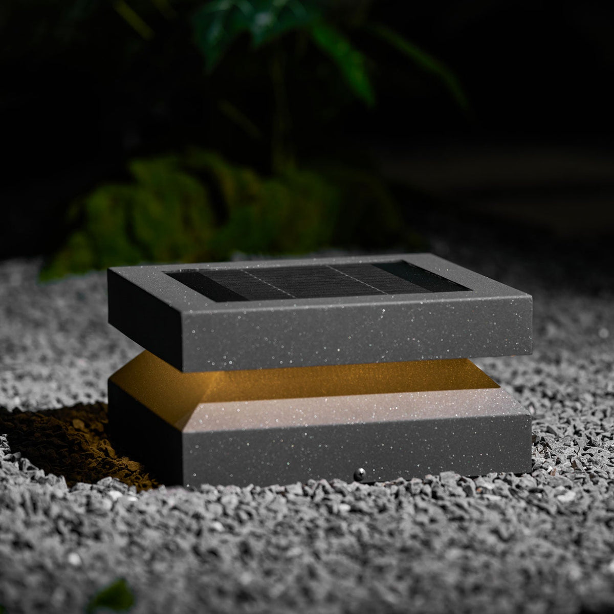 Clérachic post light resting on grey gravel at night, a warm amber glow between lid and base.