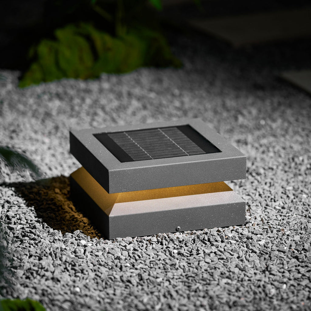 Clérachic post light on gravel lit warm, the amber glow showing between the solar lid and base.