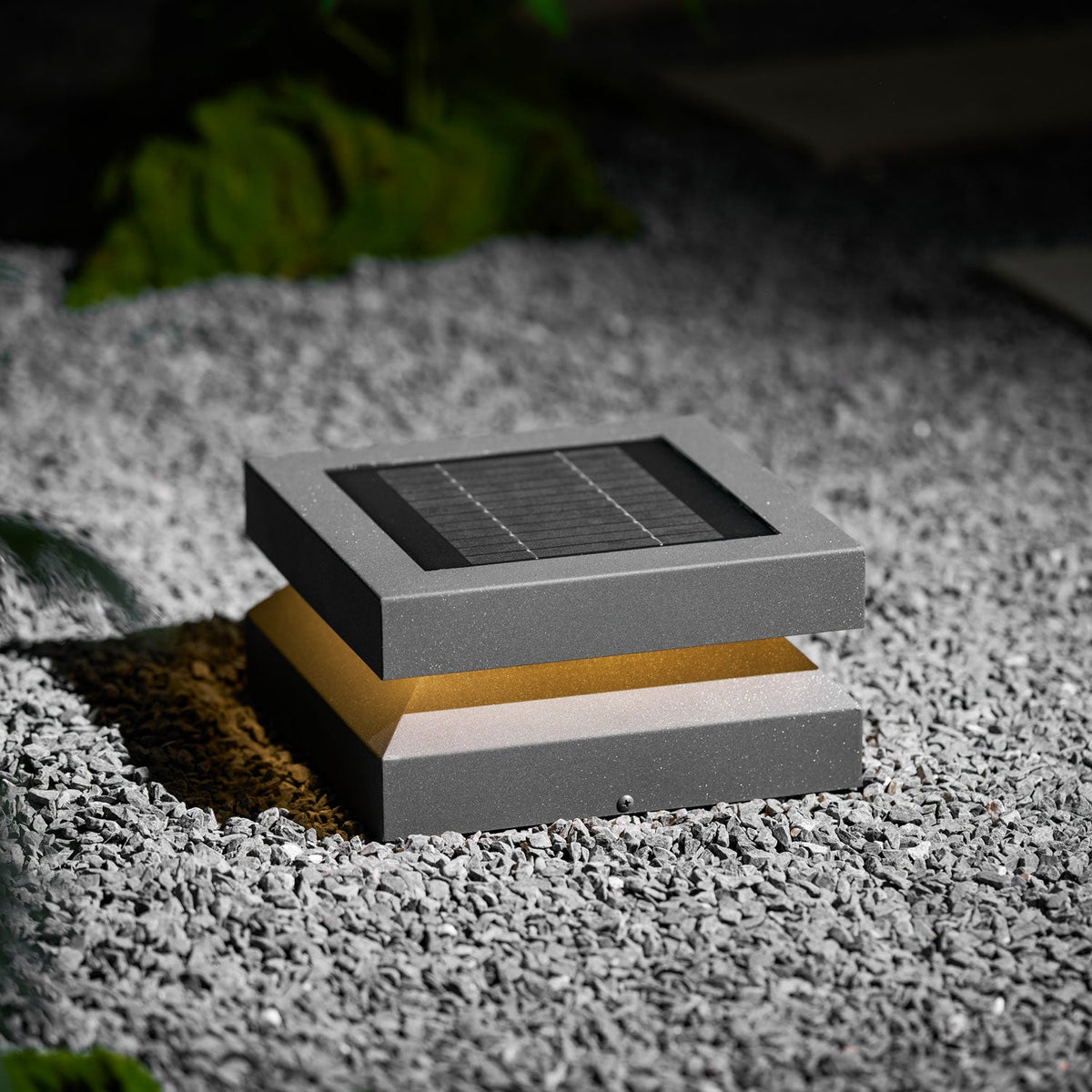 Clérachic post light on gravel lit warm, the amber glow showing between the solar lid and base.