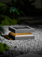 From a lower angle, a Clérachic post light on gravel glows softly beside a dark green plant.