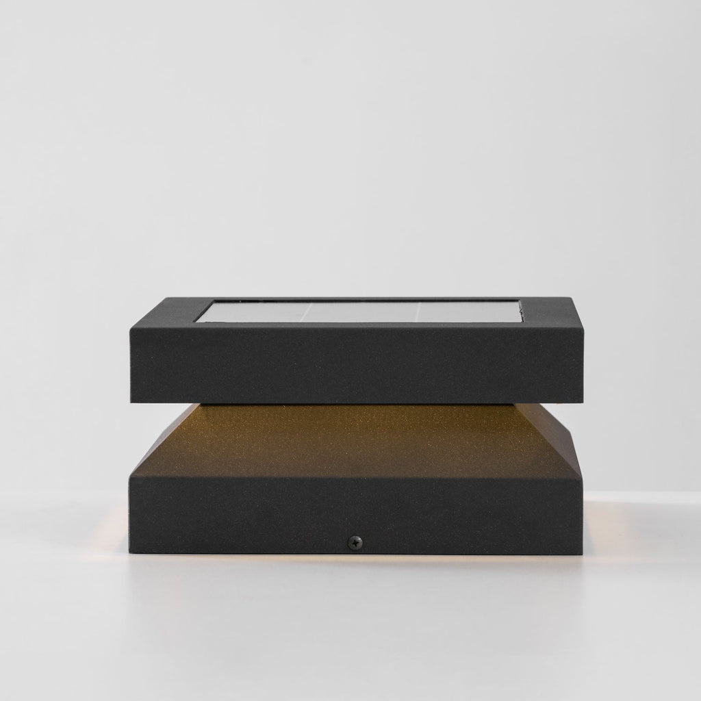 Side view of a lit Clérachic post light, a flat solar lid over a warm glow and a tapered dark base.