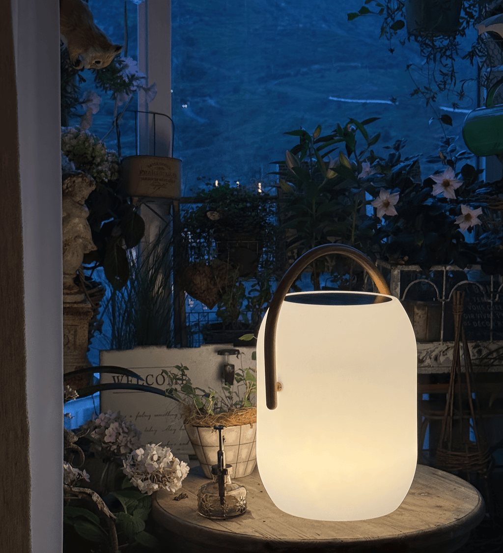 A Clérachic solar lantern glowing on a round table at dusk, its wood-grain handle arched over a dark solar panel top.