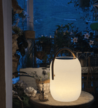 A Clérachic solar lantern glowing on a round table at dusk, its wood-grain handle arched over a dark solar panel top.