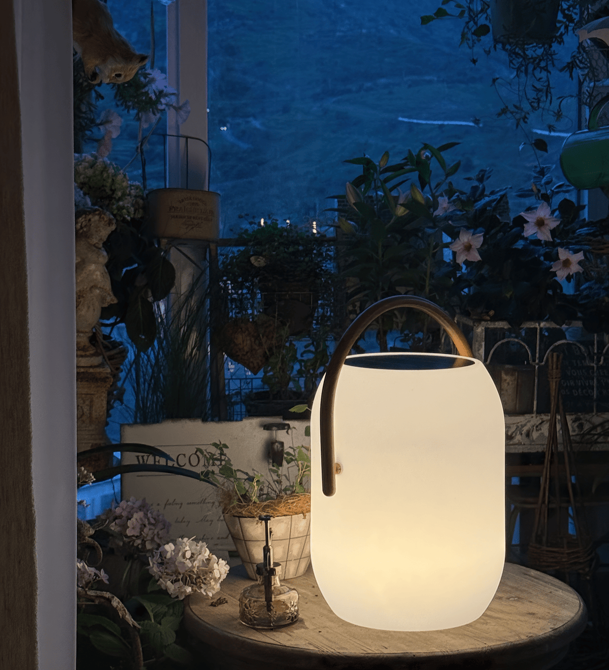 A Clérachic solar lantern glowing on a round table at dusk, its wood-grain handle arched over a dark solar panel top.