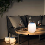 Clérachic solar lantern lit on a round wooden tray table between two wine glasses, with two more lanterns on the floor beside the sofa.