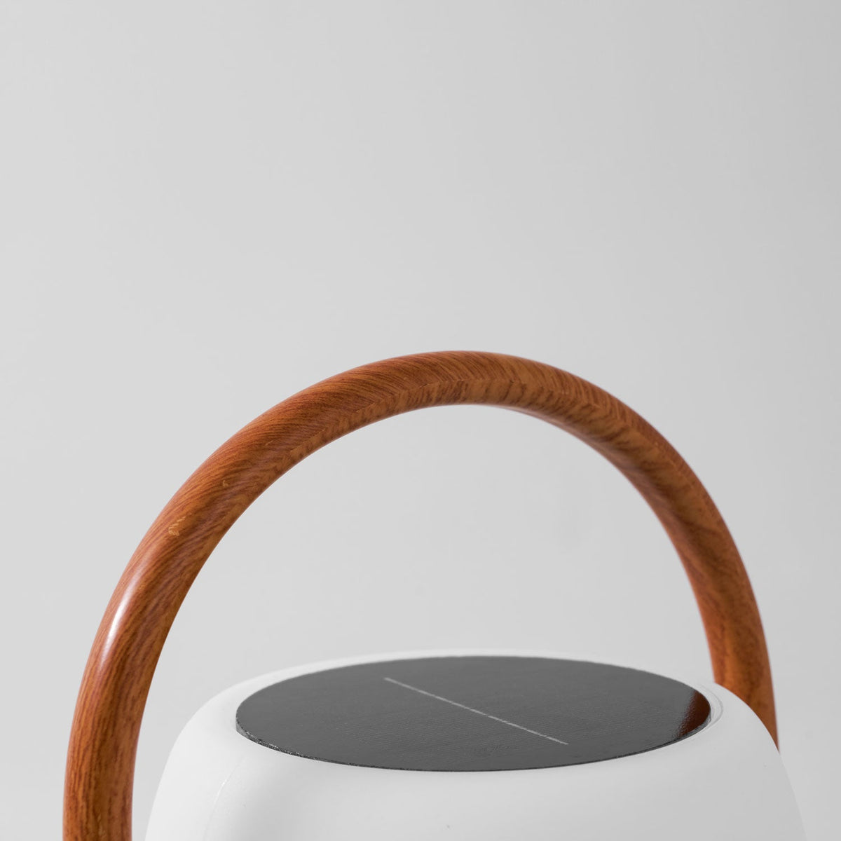 Close view of the dark solar panel on top of this Clérachic lantern, with the wood-grain handle curving over it.
