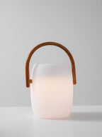 A Clérachic lantern with a soft warm glow rising from the base of its white body, handle upright, on a pale backdrop.