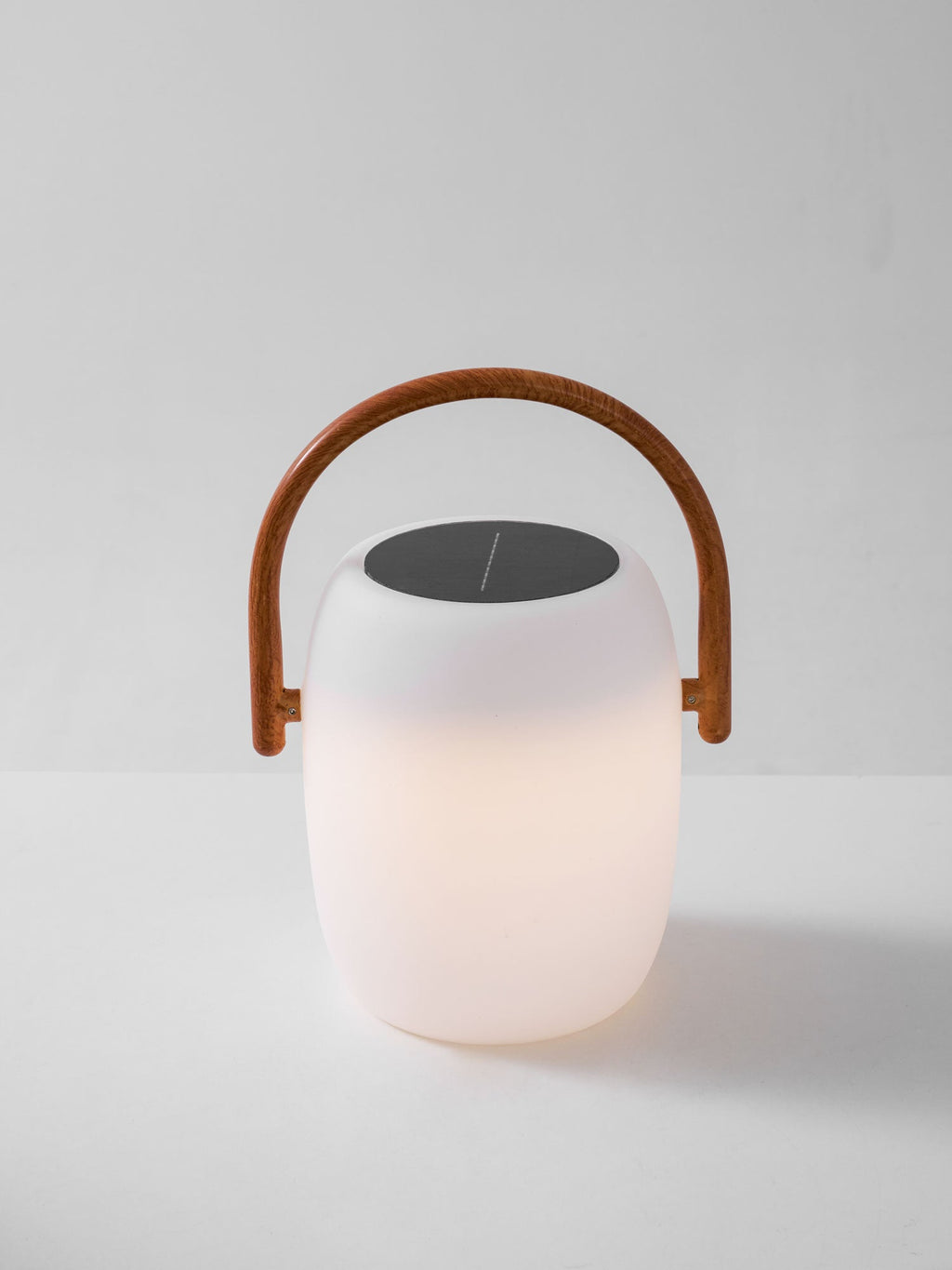 Smaller Clérachic solar lantern with a warm glow in the lower half of its white shell and a wood-grain handle.
