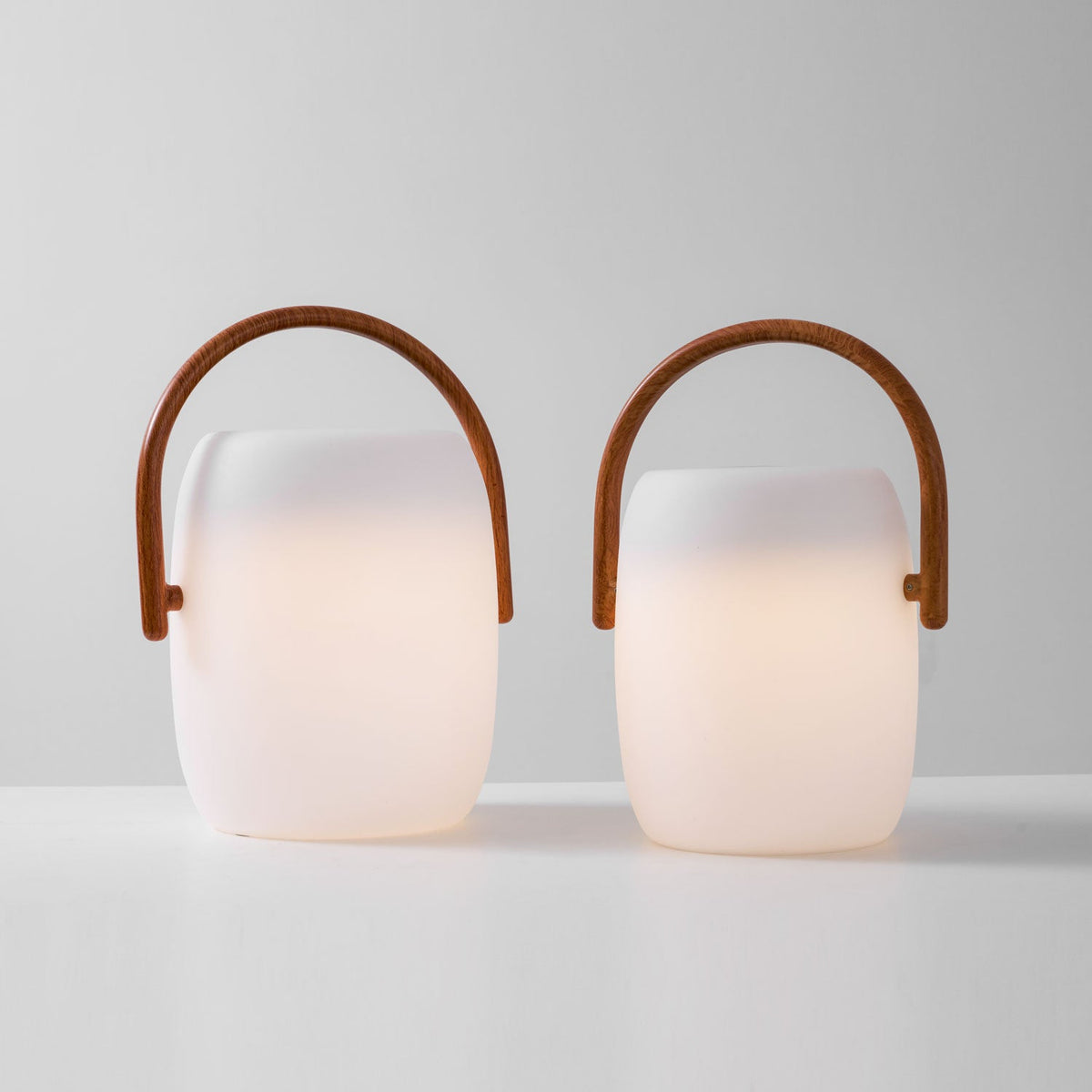 Pair of Clérachic lanterns in two sizes, switched on, the warm light filling the lower part of each white body.