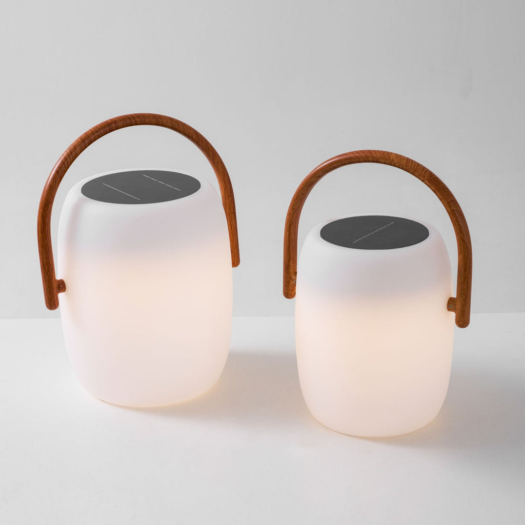 Two Clérachic lanterns lit side by side, the glow fading upward toward their dark solar tops and wood-grain handles.