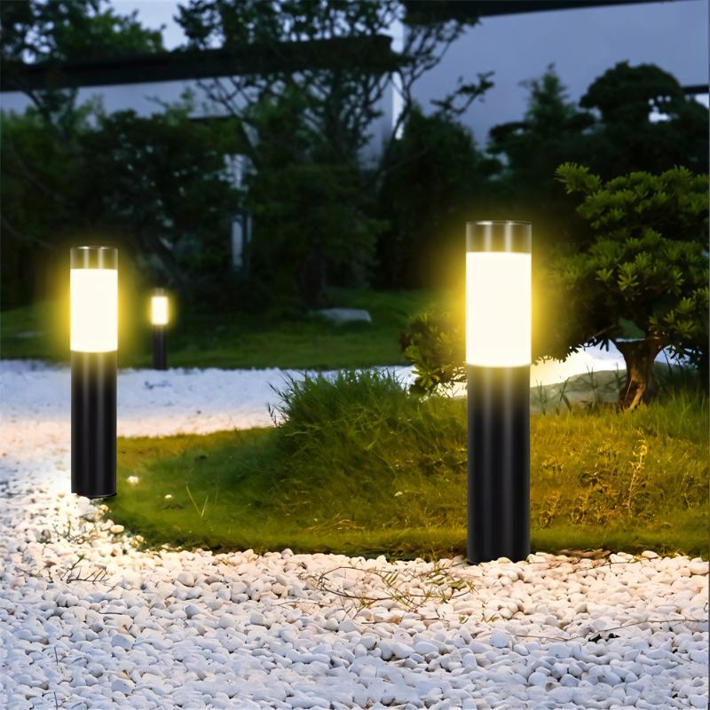 Two Clérachic black solar path lights with frosted white bands glowing warm beside white pebbles and a garden lawn.