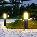 Two Clérachic black solar path lights with frosted white bands glowing warm beside white pebbles and a garden lawn.